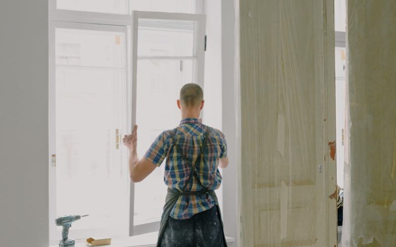 Full-length view of a handyman fixing a modern window in a bright room.
