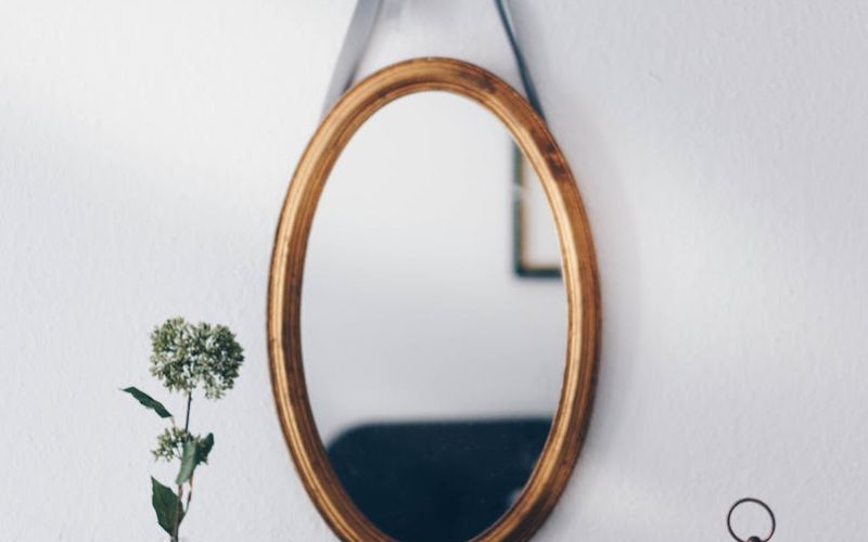 A stylish interior setup featuring a hanging oval mirror with decorative elements on a wooden table.