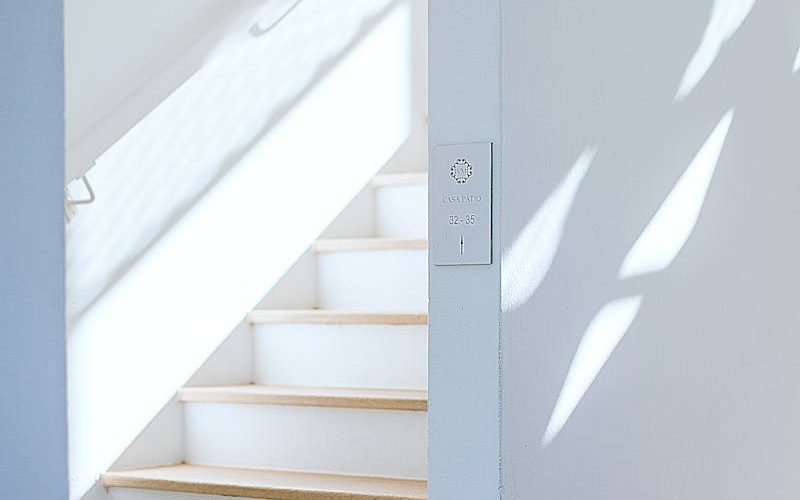 Bright minimalist interior featuring a white staircase with an arch and natural light casting shadows.