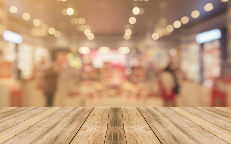 Empty wooden table with blurred shopping mall background and bokeh lights.